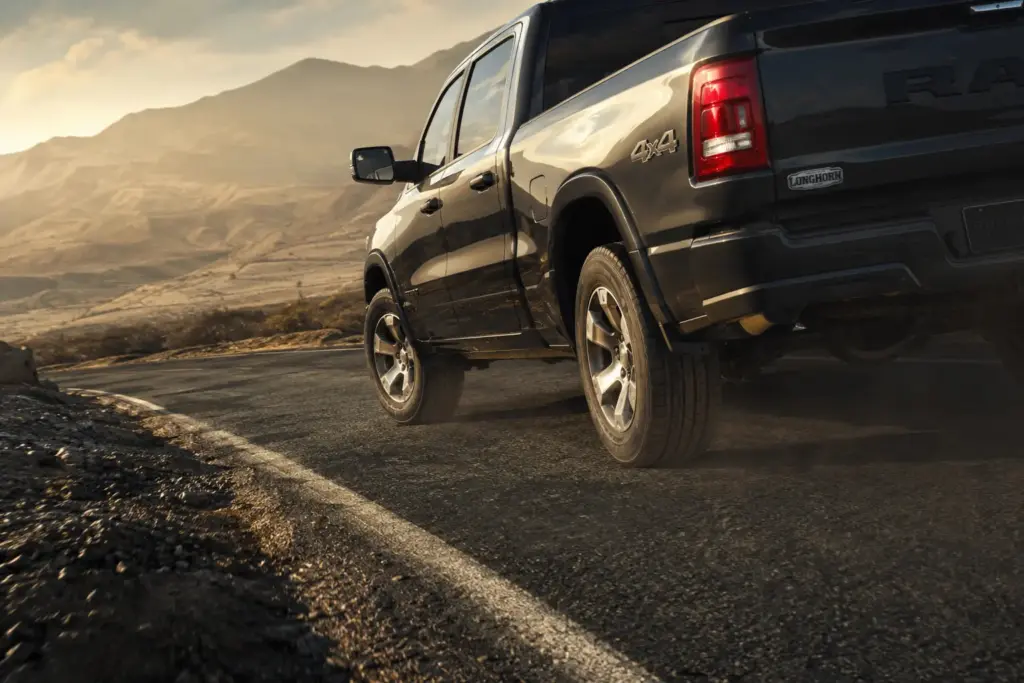 Black 4x4 pickup truck driving along a dusty desert road with mountains in the background at sunset.